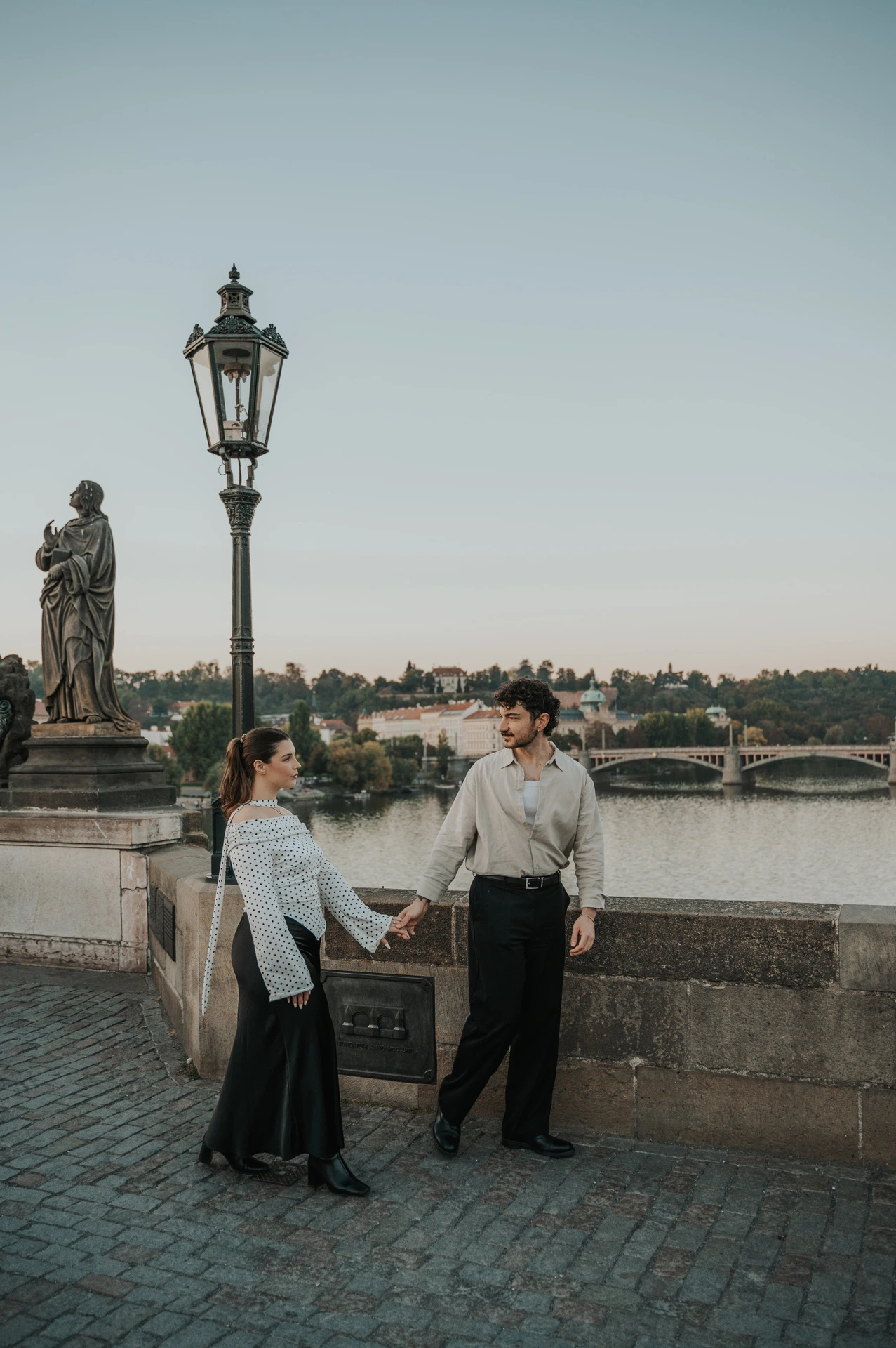 Couple holding hands beneath the bridge lamp during a couple photoshoot in Prague.