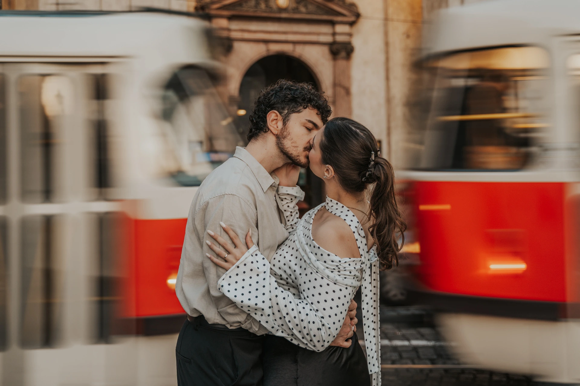 Couple kissing with a passing red tram behind them during a couple photoshoot in Prague.