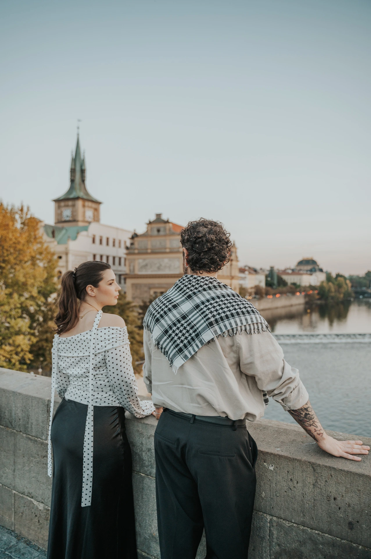 Couple looking over the bridge wall towards the water during a couple photoshoot in Prague.