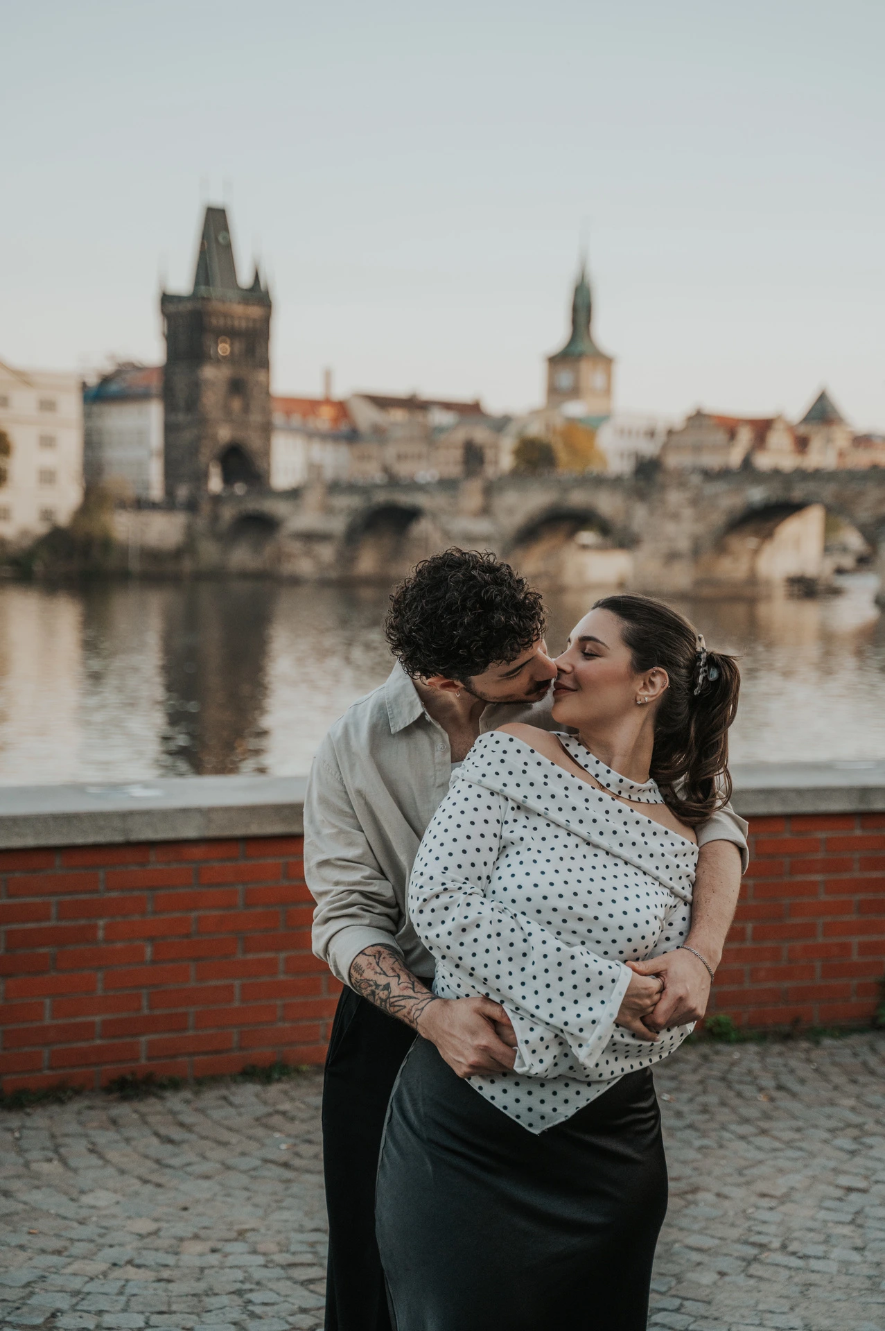 Couple sharing a kiss beside the riverside wall during a couple photoshoot in Prague.