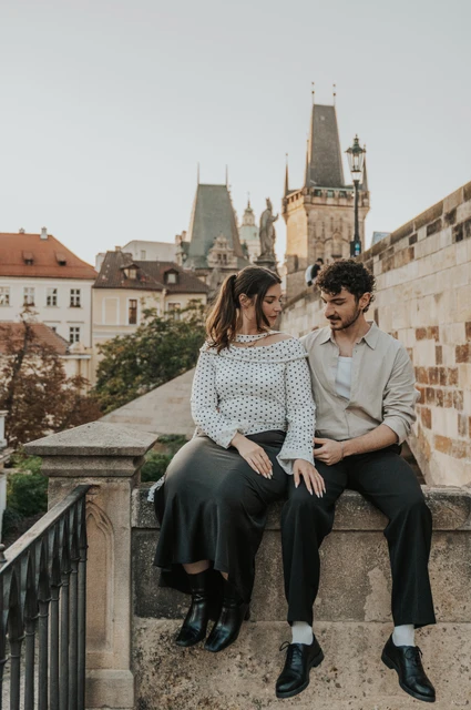 Prague couple photoshoot: couple sitting together on the stone railing by Charles Bridge. Couple sitting together on the stone railing by Charles Bridge during a couple photoshoot in Prague.