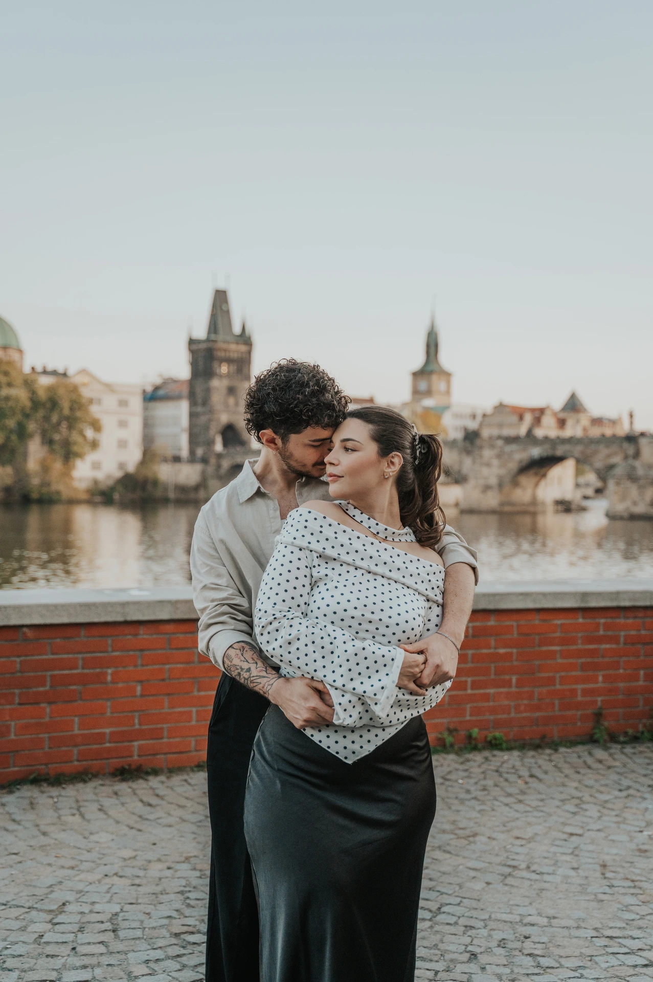 Couple smiling as they hold each other by the brick wall during a couple photoshoot in Prague.