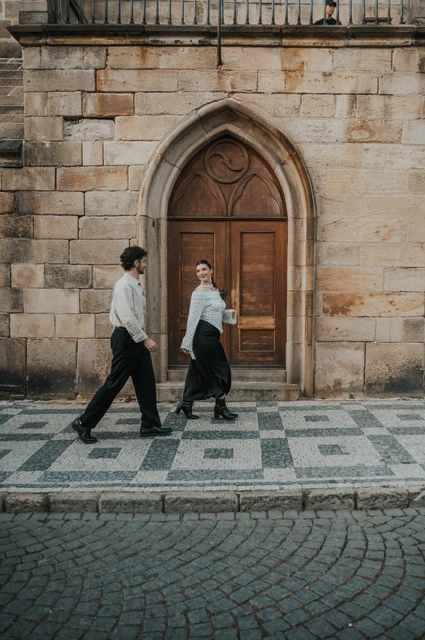 Prague couple photoshoot: couple smiling as they walk beside the bridge wall. Couple smiling as they walk beside the bridge wall during a couple photoshoot in Prague.