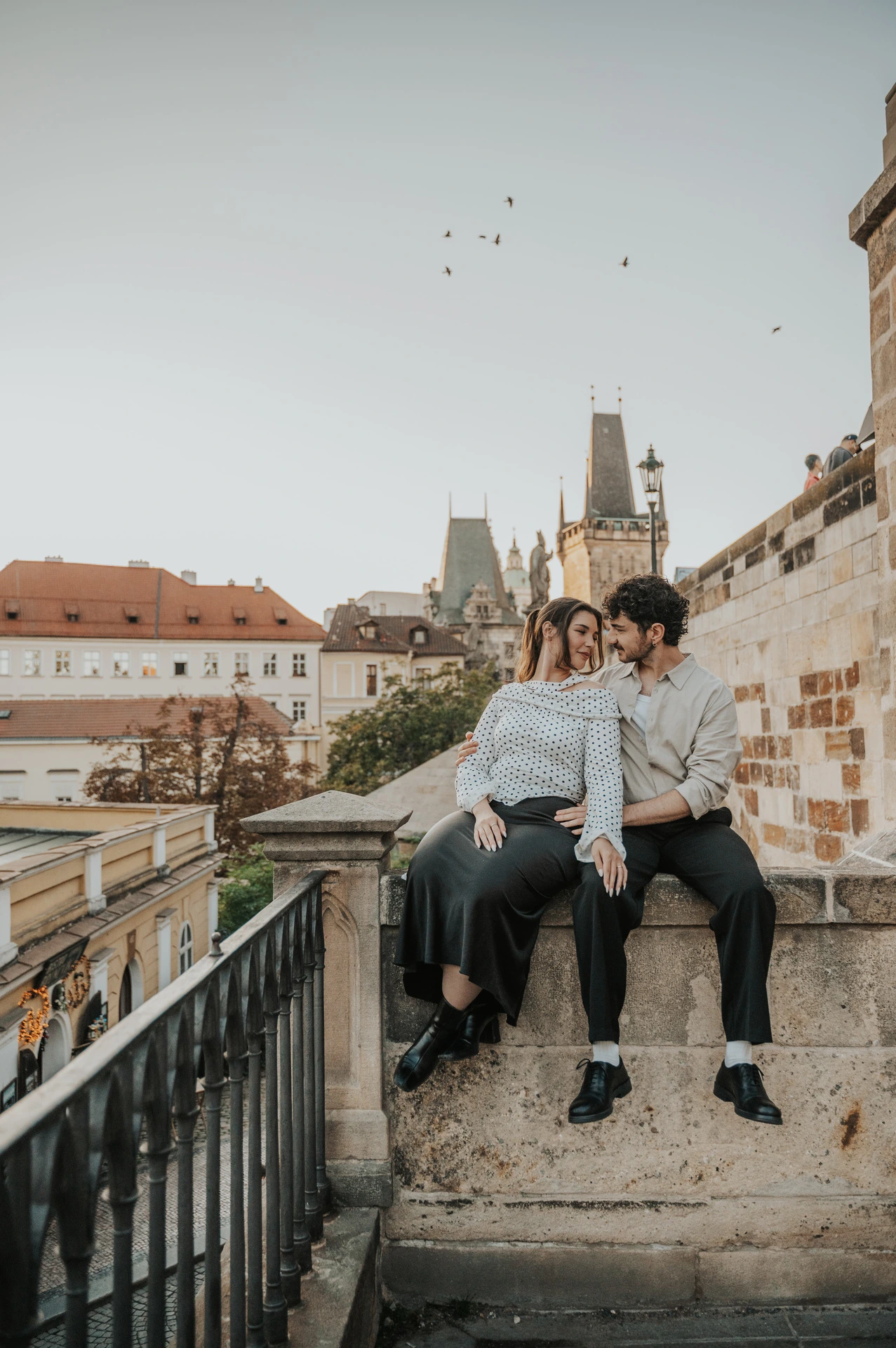 Couple smiling on a stone ledge above the steps during a couple photoshoot in Prague.
