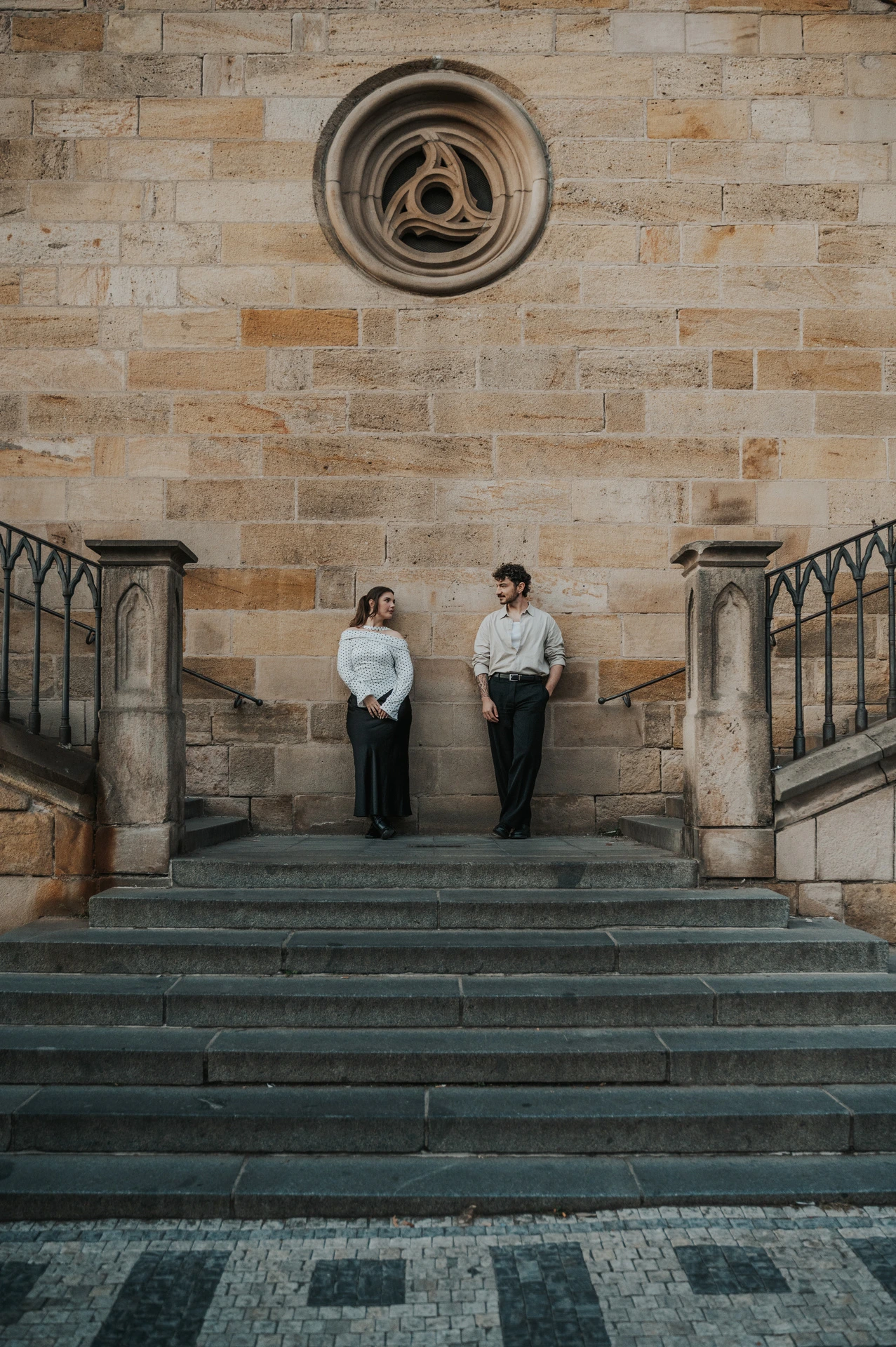 Couple smiling together beneath the round stone window during a couple photoshoot in Prague.