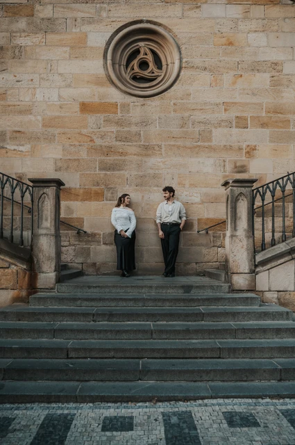 Prague couple photoshoot: couple smiling together beneath the round stone window. Couple smiling together beneath the round stone window during a couple photoshoot in Prague.