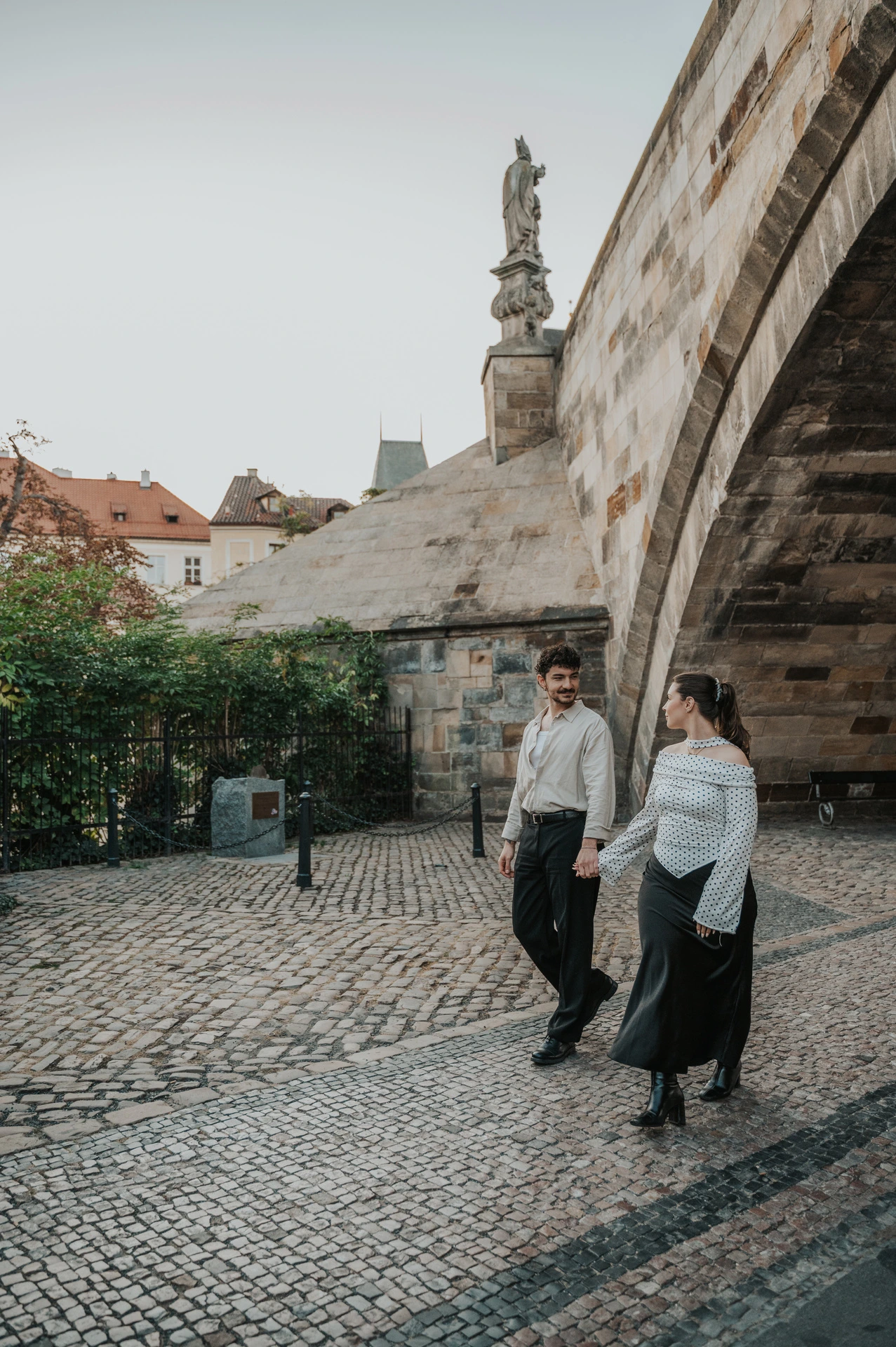 Couple standing together beneath a Charles Bridge arch during a couple photoshoot in Prague.