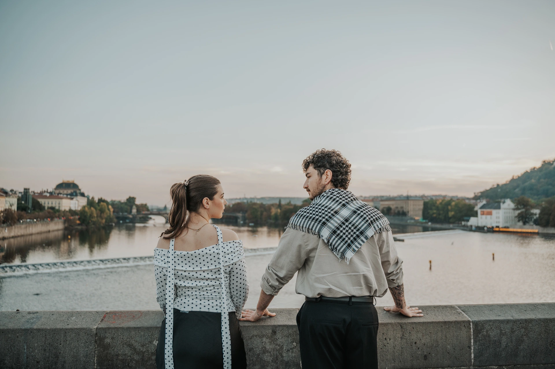 Couple turning back towards each other above the river during a couple photoshoot in Prague.