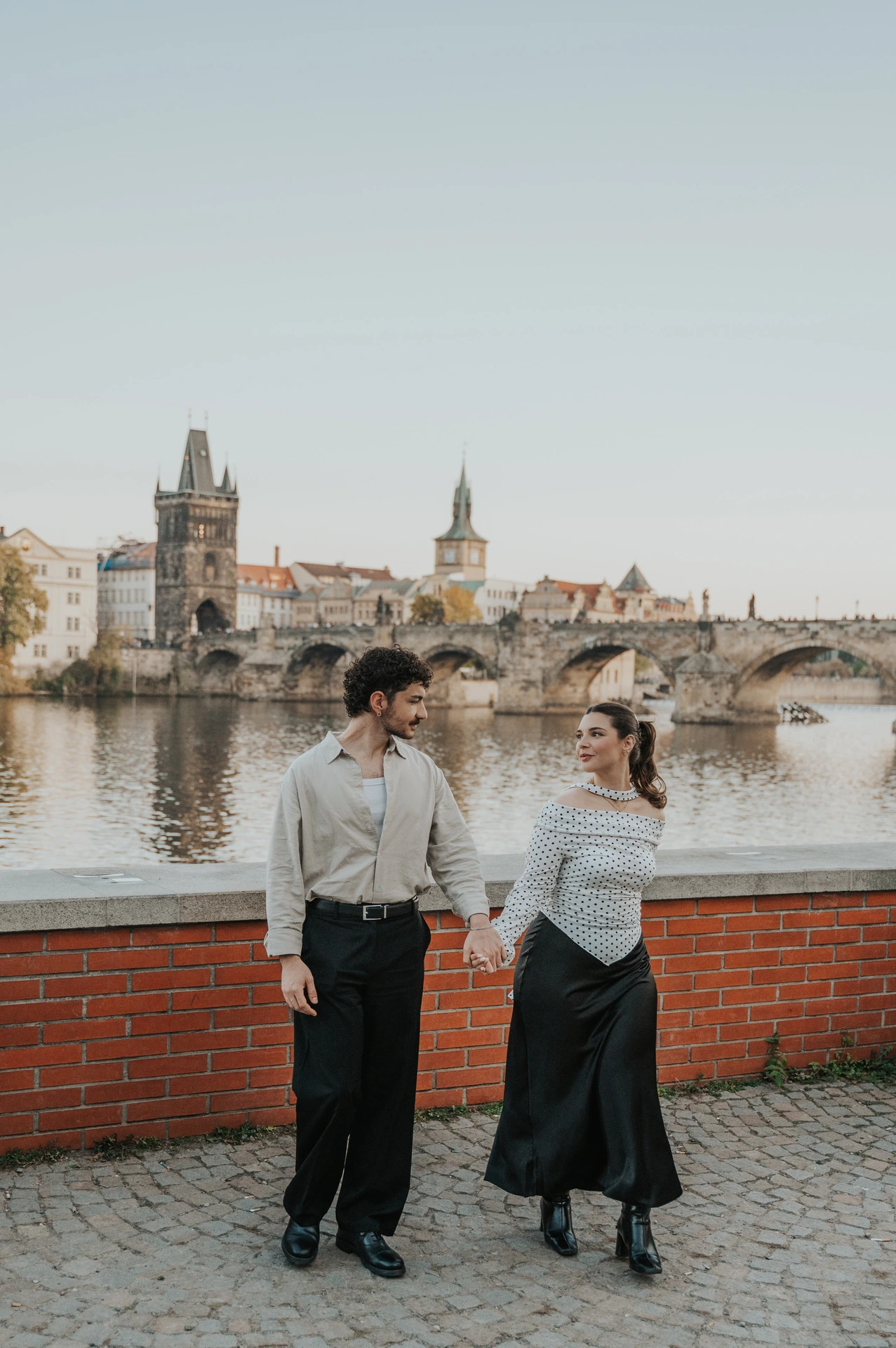 Couple walking hand in hand along the riverside pavement during a couple photoshoot in Prague.
