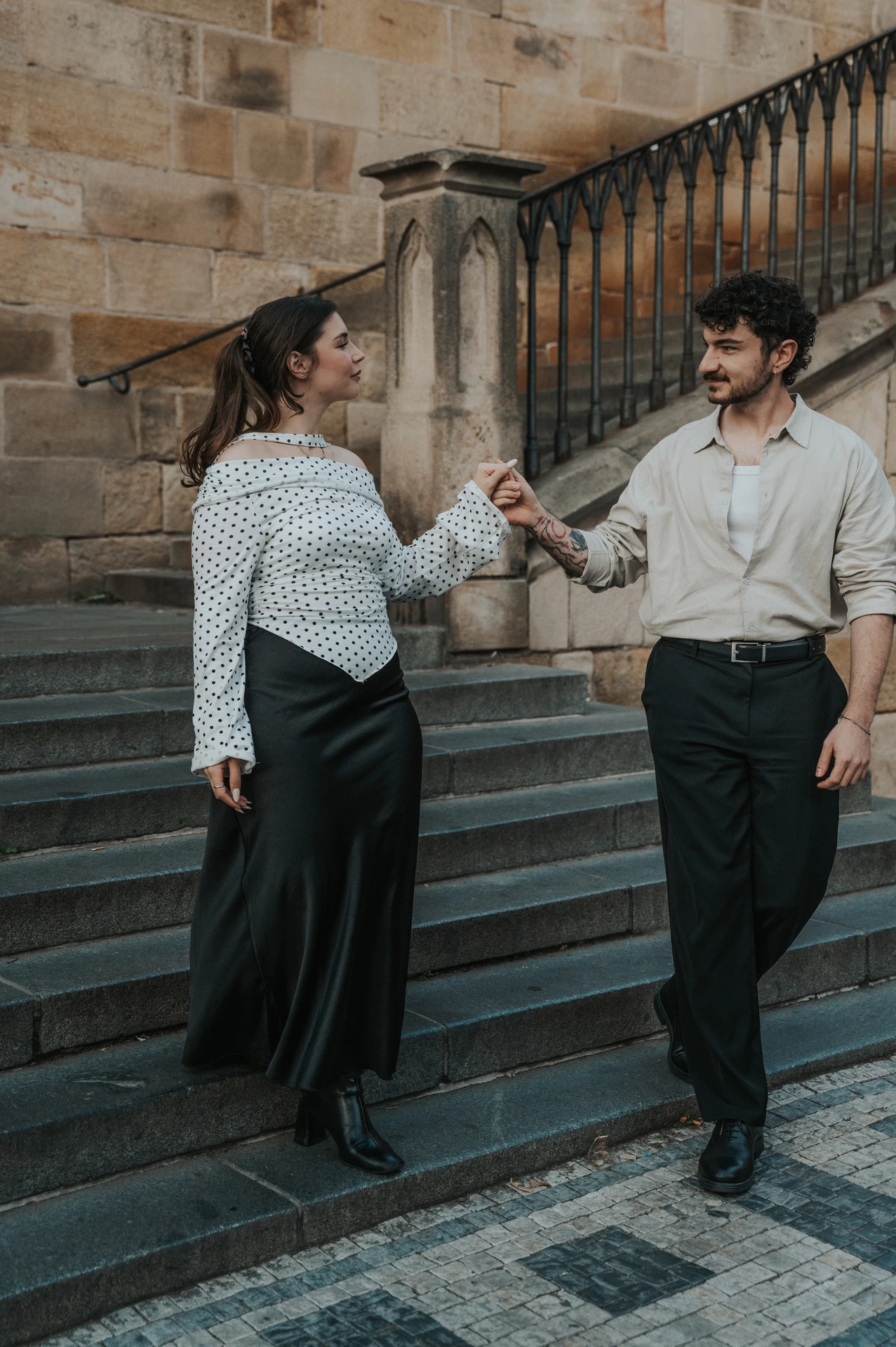 Couple walking hand in hand down the bridge-side steps during a couple photoshoot in Prague.
