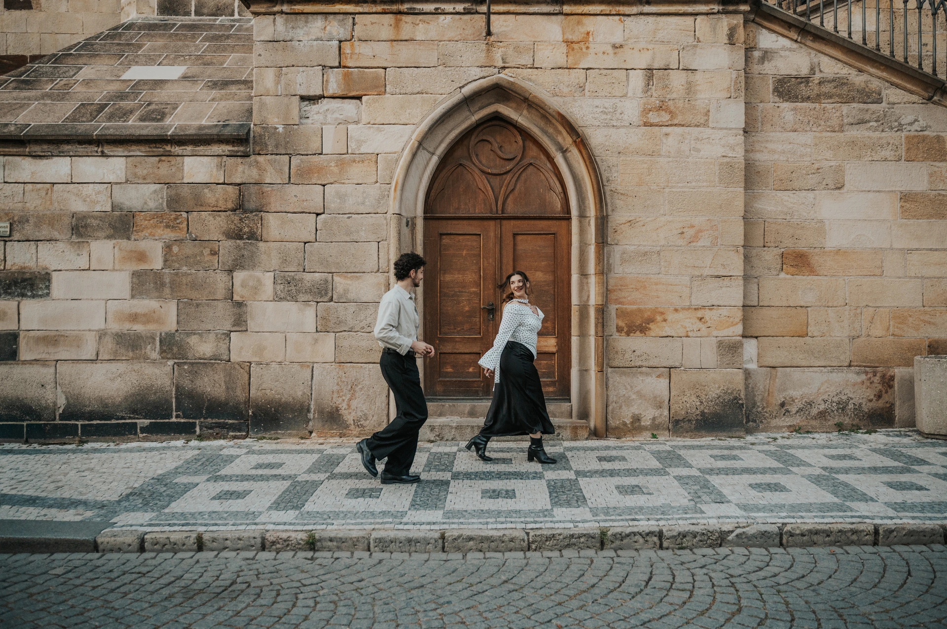 Couple walking past an arched wooden doorway in Kampa during a couple photoshoot in Prague.