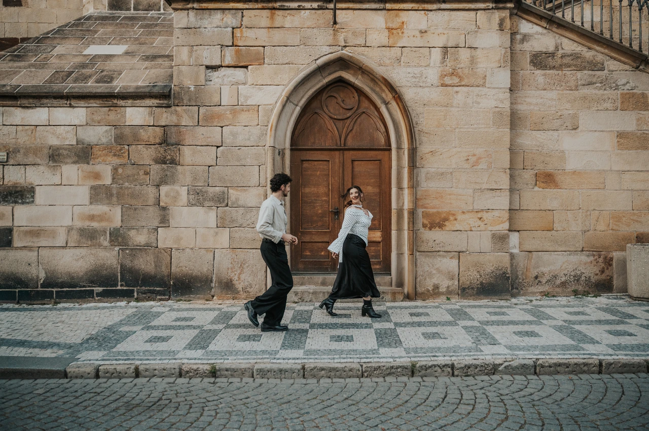 Prague couple photoshoot: couple walking past an arched wooden doorway in Kampa. Couple walking past an arched wooden doorway in Kampa during a couple photoshoot in Prague.