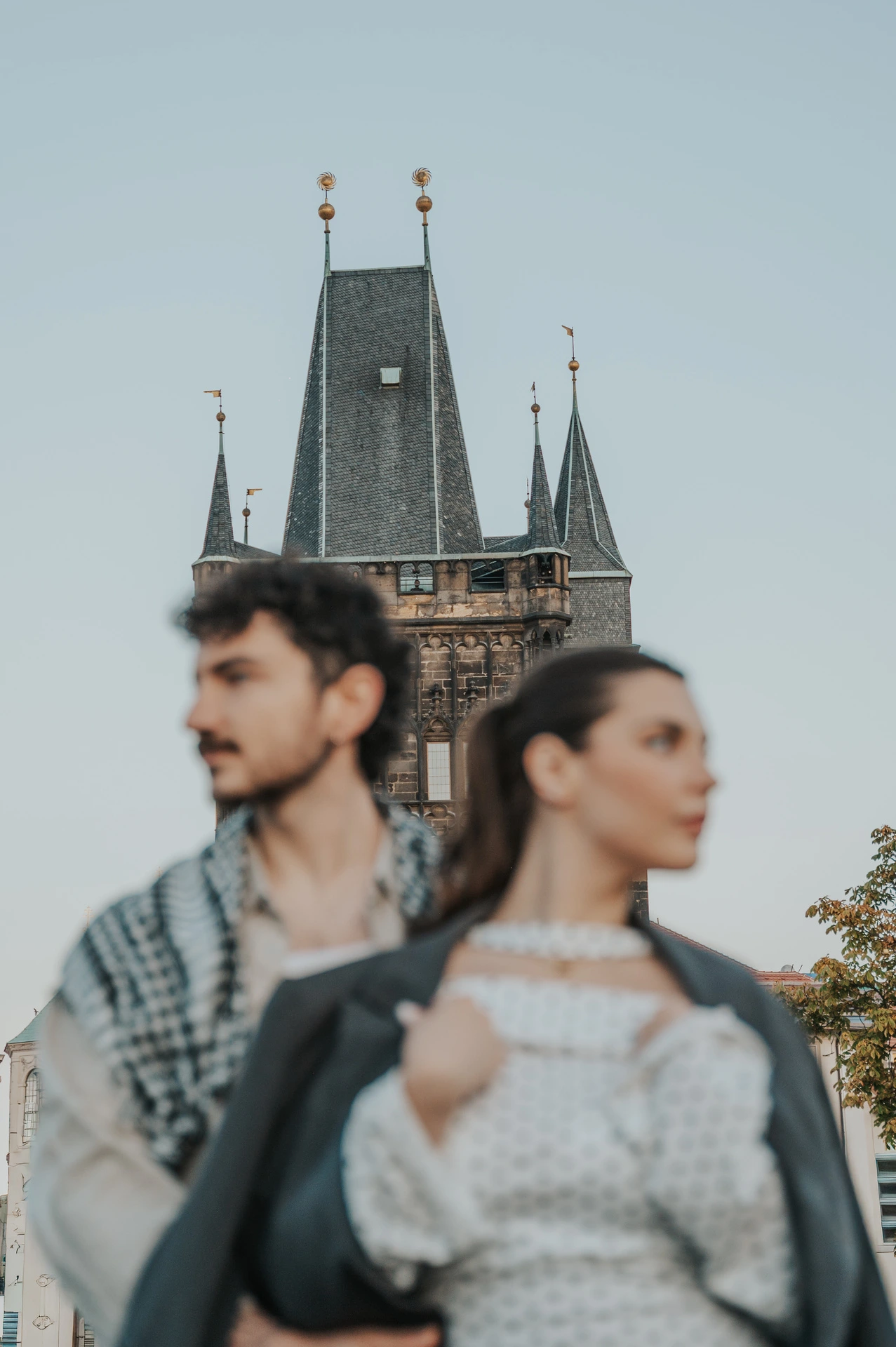 Couple wearing a checked wrap by the bridge tower during a couple photoshoot in Prague.