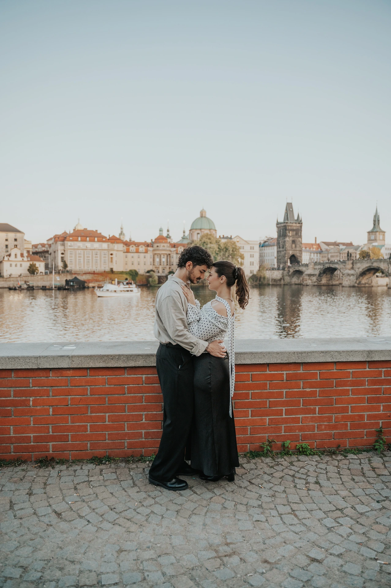 Wide portrait of the couple kissing above the Vltava during a couple photoshoot in Prague.