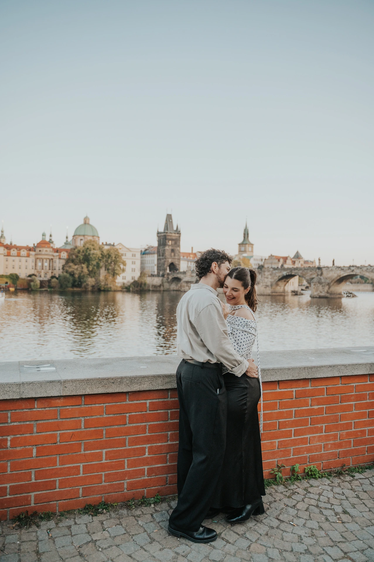 Wide view of the couple embracing beside the brick wall during a couple photoshoot in Prague.