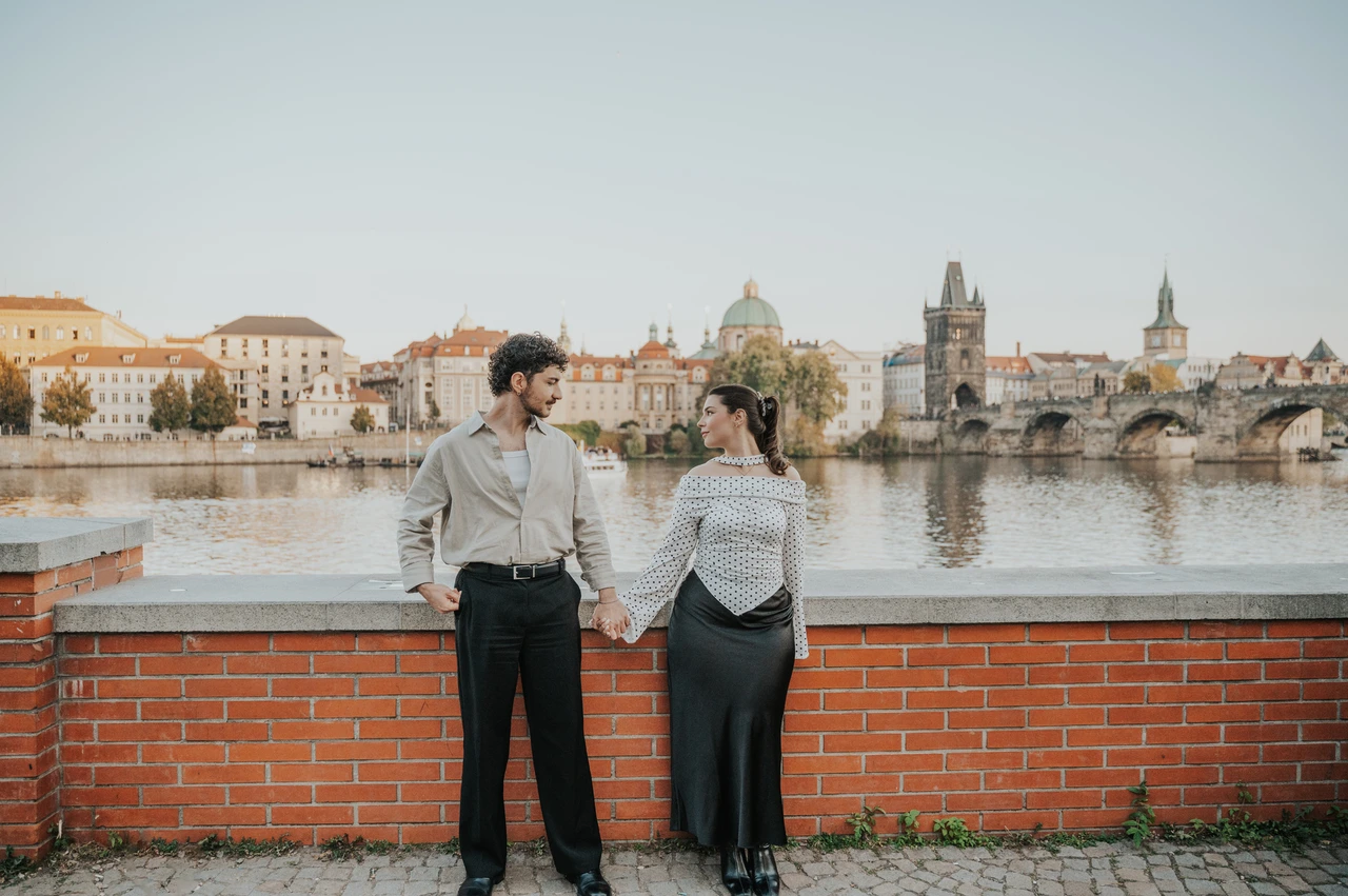 Prague couple photoshoot: wide view of the couple standing beside the river. Wide view of the couple standing beside the river during a couple photoshoot in Prague.