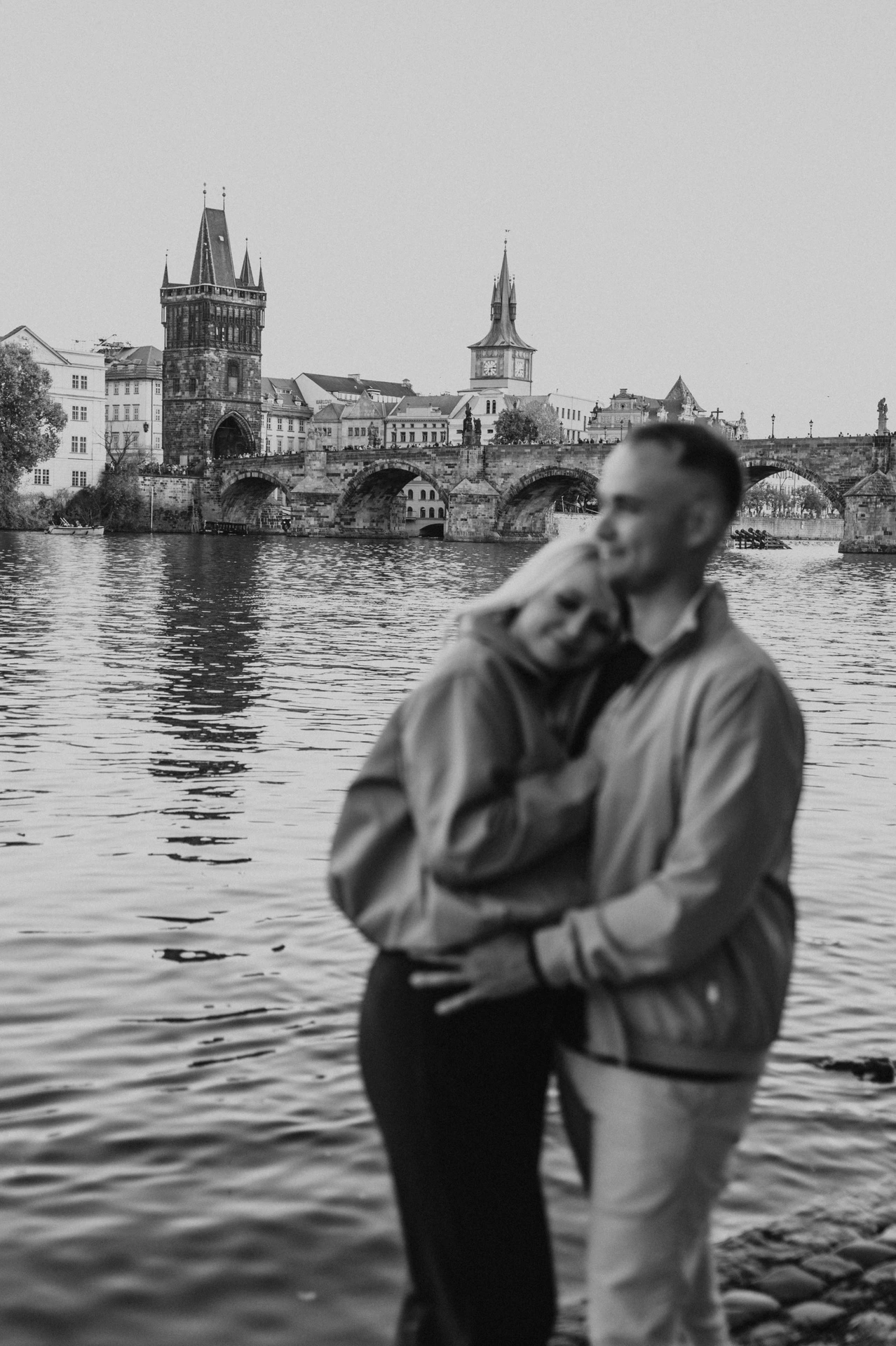 Black and white embrace beside the Vltava during a couple photoshoot in Prague.