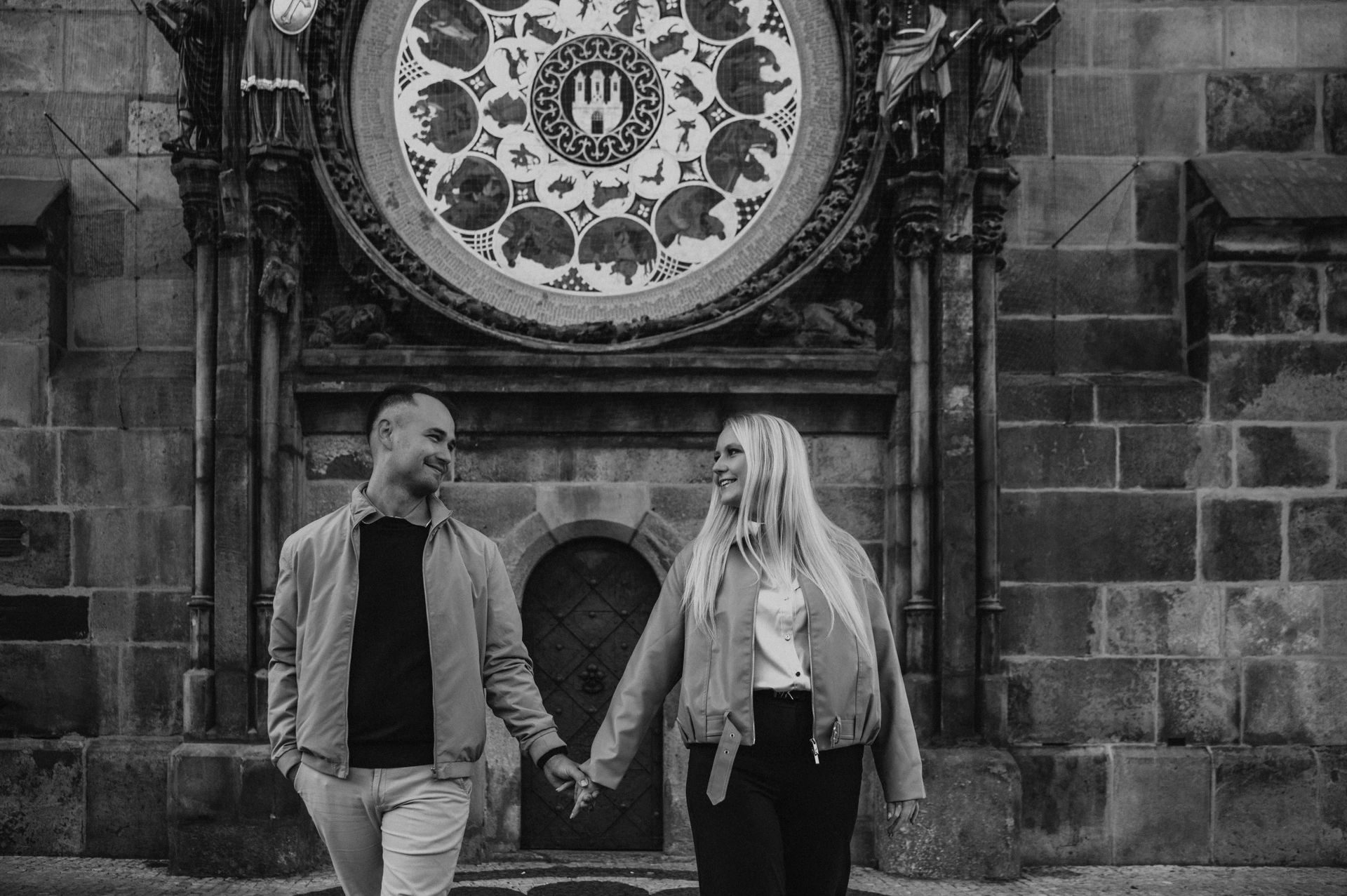 Black and white portrait of the couple below the clock during a couple photoshoot in Prague.