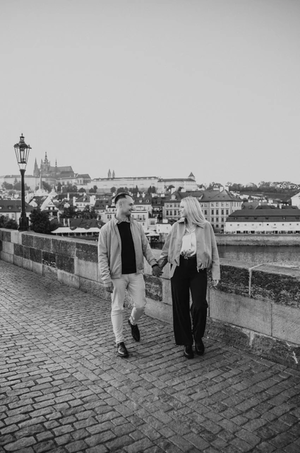 Prague couple photoshoot: black and white portrait of the couple walking on the bridge. Black and white portrait of the couple walking on the bridge during a couple photoshoot in Prague.