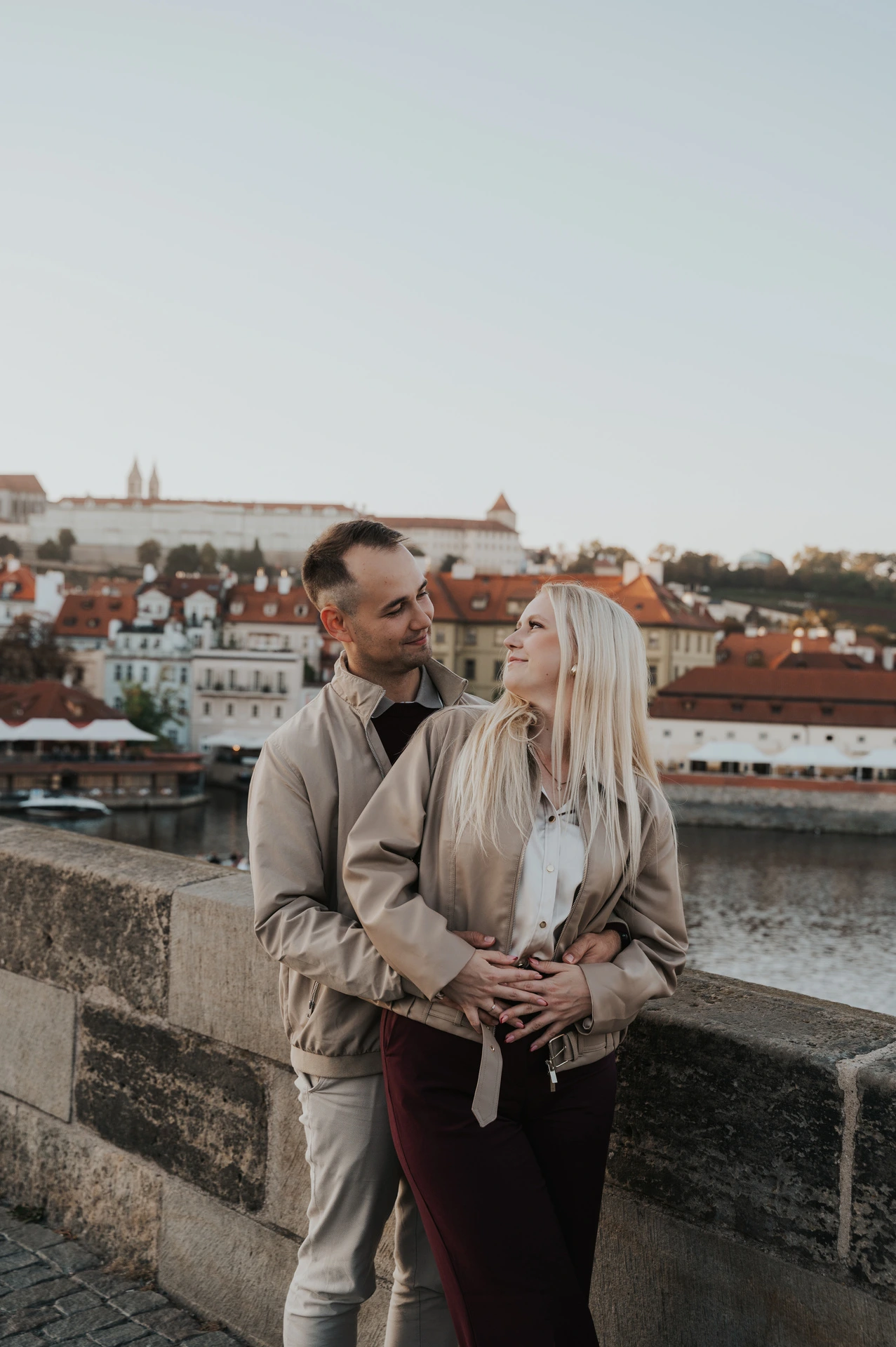 Couple cuddling with old rooftops behind them during a couple photoshoot in Prague.