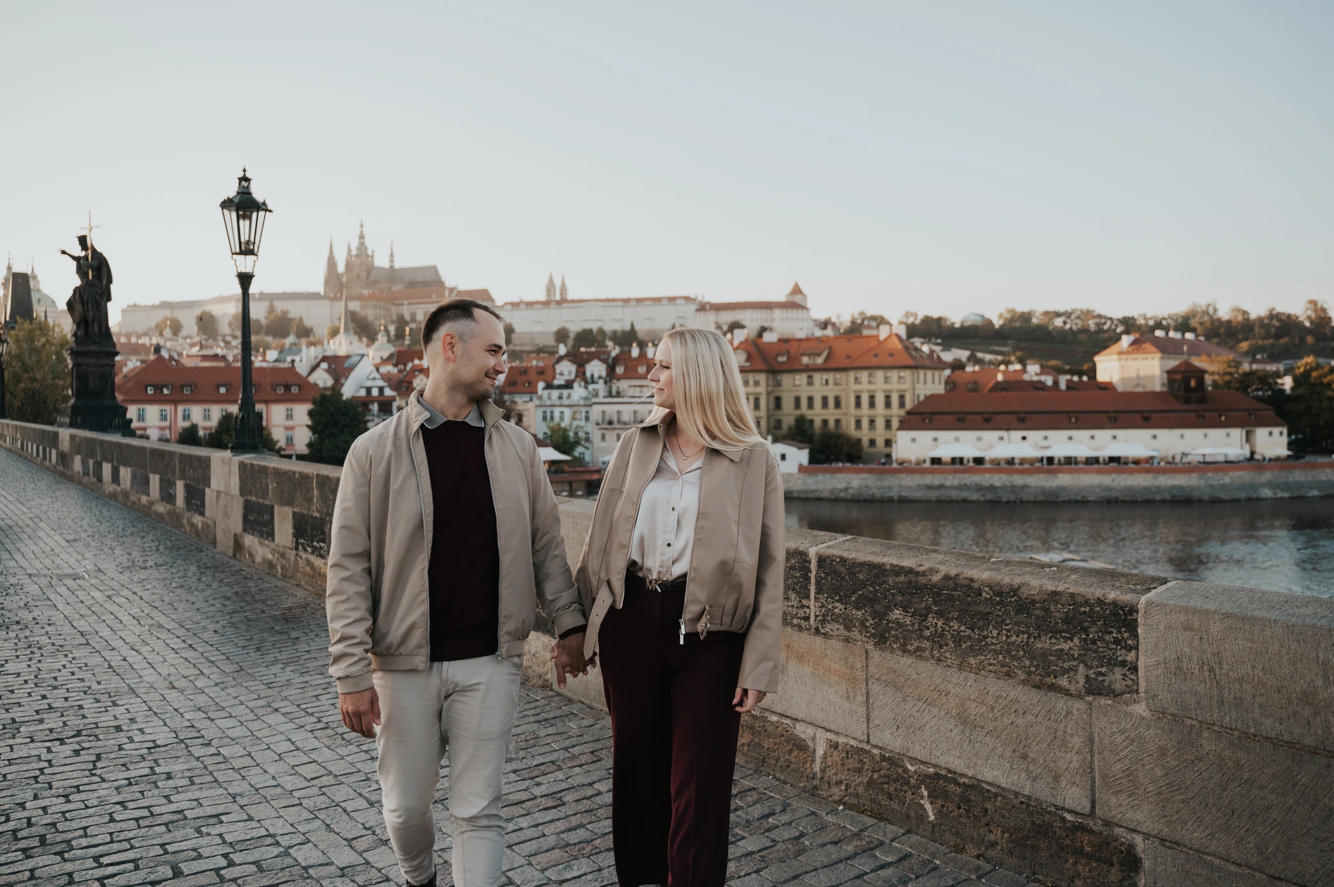 Couple exchanging smiles as they walk along Charles Bridge during a couple photoshoot in Prague.