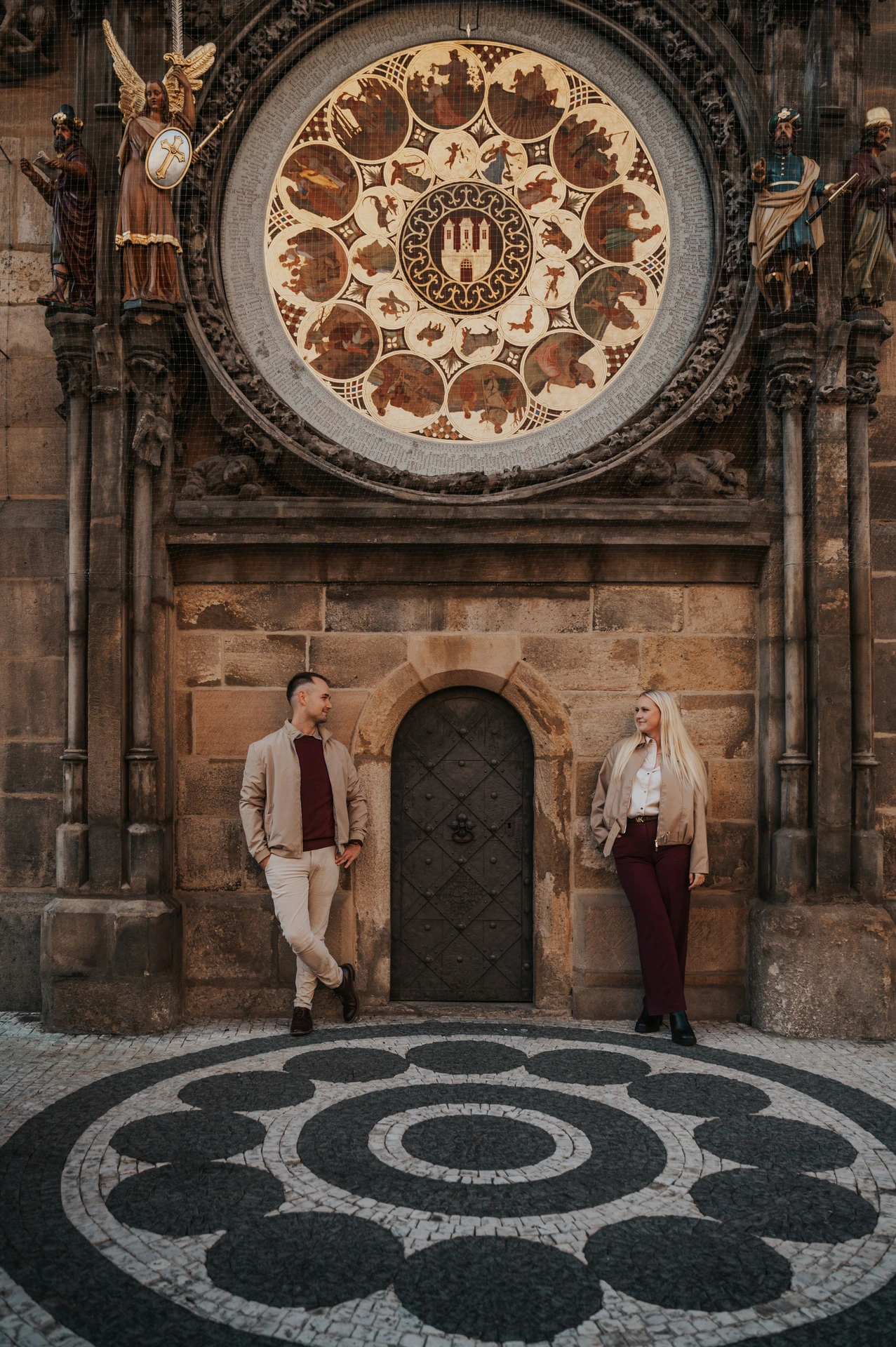 Couple holding hands under the decorated clock face during a couple photoshoot in Prague.