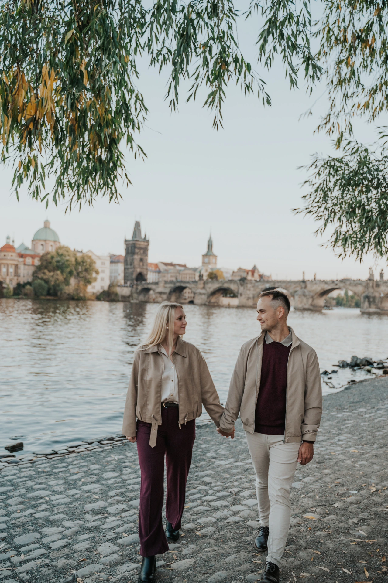Couple holding hands under the riverside willow during a couple photoshoot in Prague.