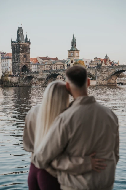 Prague couple photoshoot: couple looking across the water towards Charles Bridge. Couple looking across the water towards Charles Bridge during a couple photoshoot in Prague.