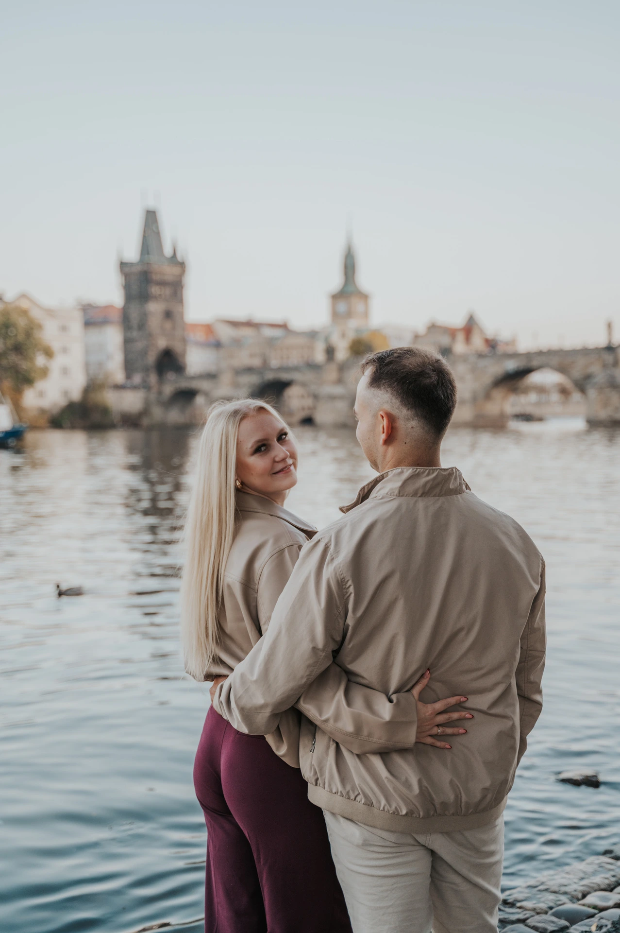 Couple looking back over their shoulders on the riverbank during a couple photoshoot in Prague.