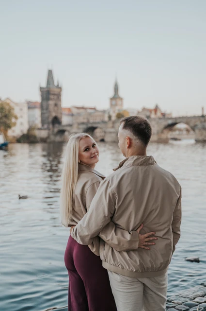 Prague couple photoshoot: couple looking back over their shoulders on the riverbank. Couple looking back over their shoulders on the riverbank during a couple photoshoot in Prague.