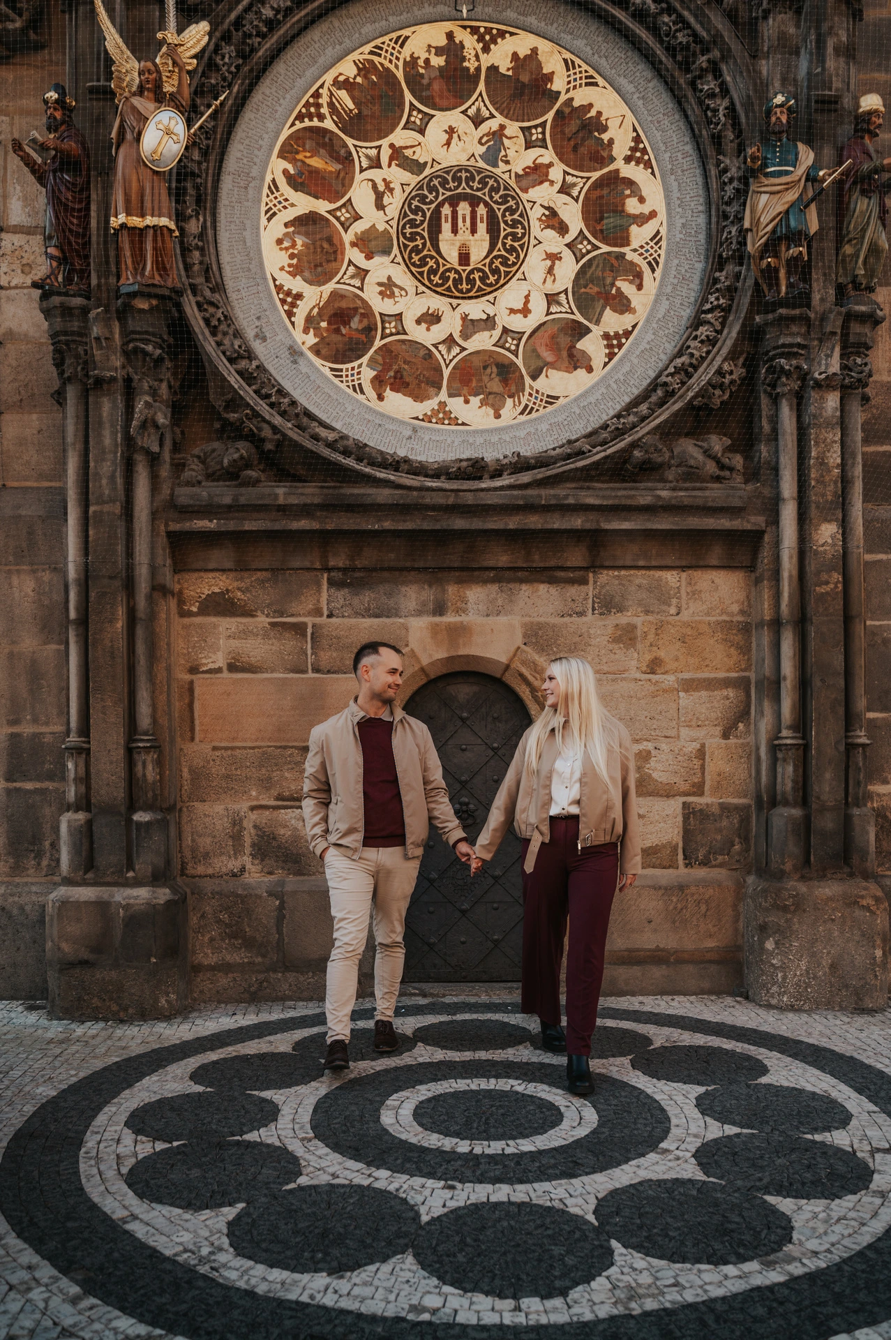Couple reaching towards each other at the Astronomical Clock during a couple photoshoot in Prague.