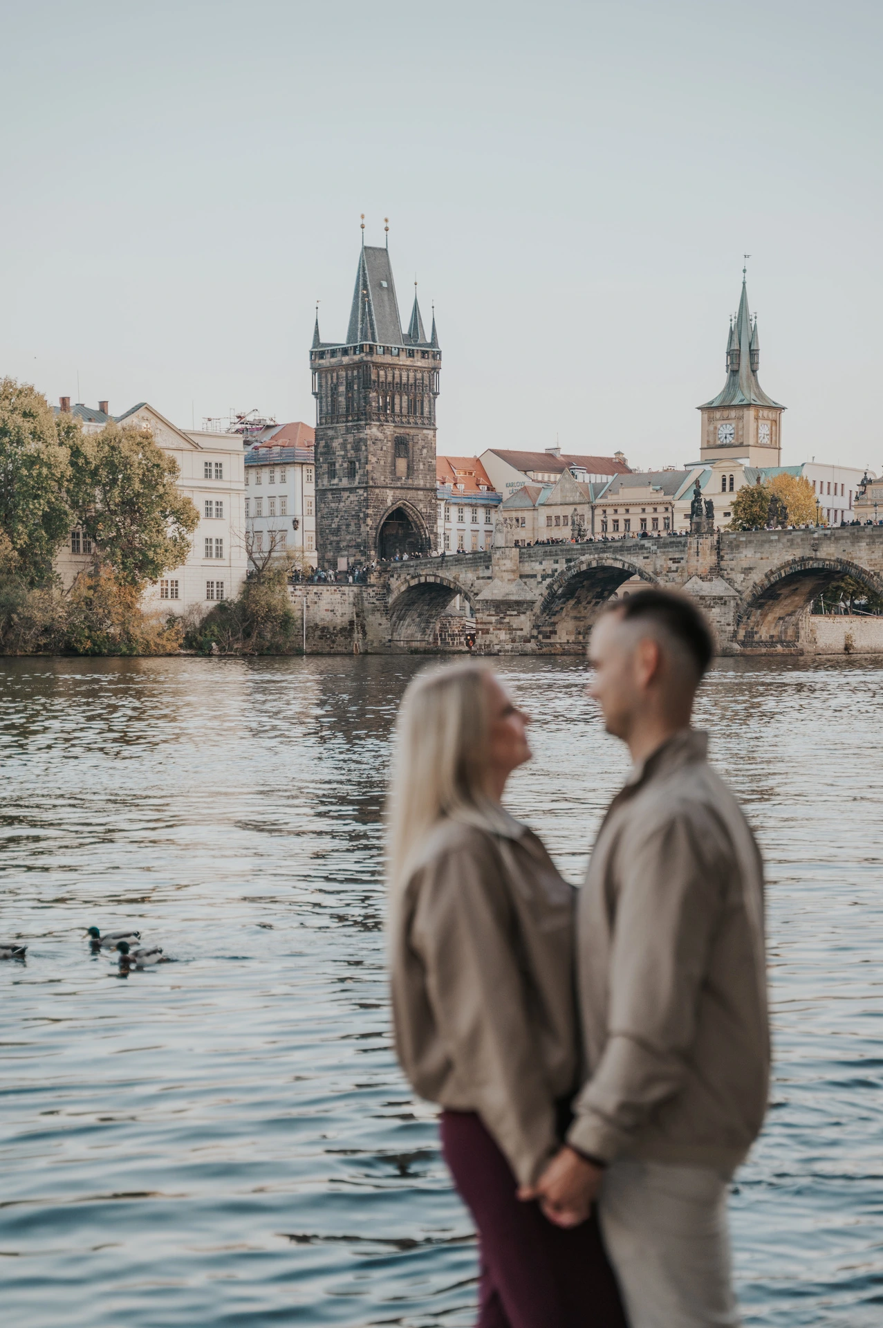 Couple standing close with the bridge reflected in the water during a couple photoshoot in Prague.