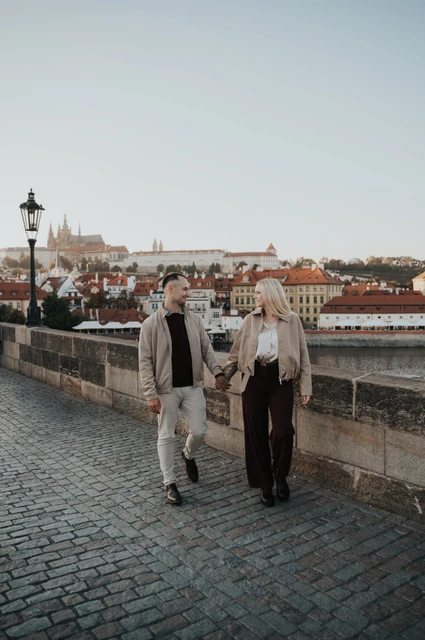 Prague couple photoshoot: couple walking hand in hand on Charles Bridge. Couple walking hand in hand on Charles Bridge during a couple photoshoot in Prague.