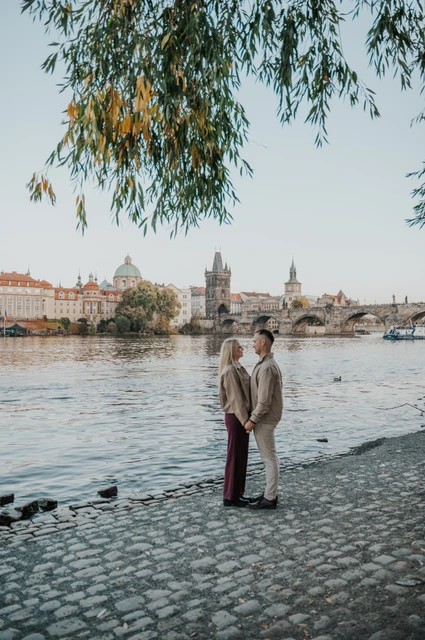 Wide portrait of the couple beneath willow branches during a couple photoshoot in Prague.