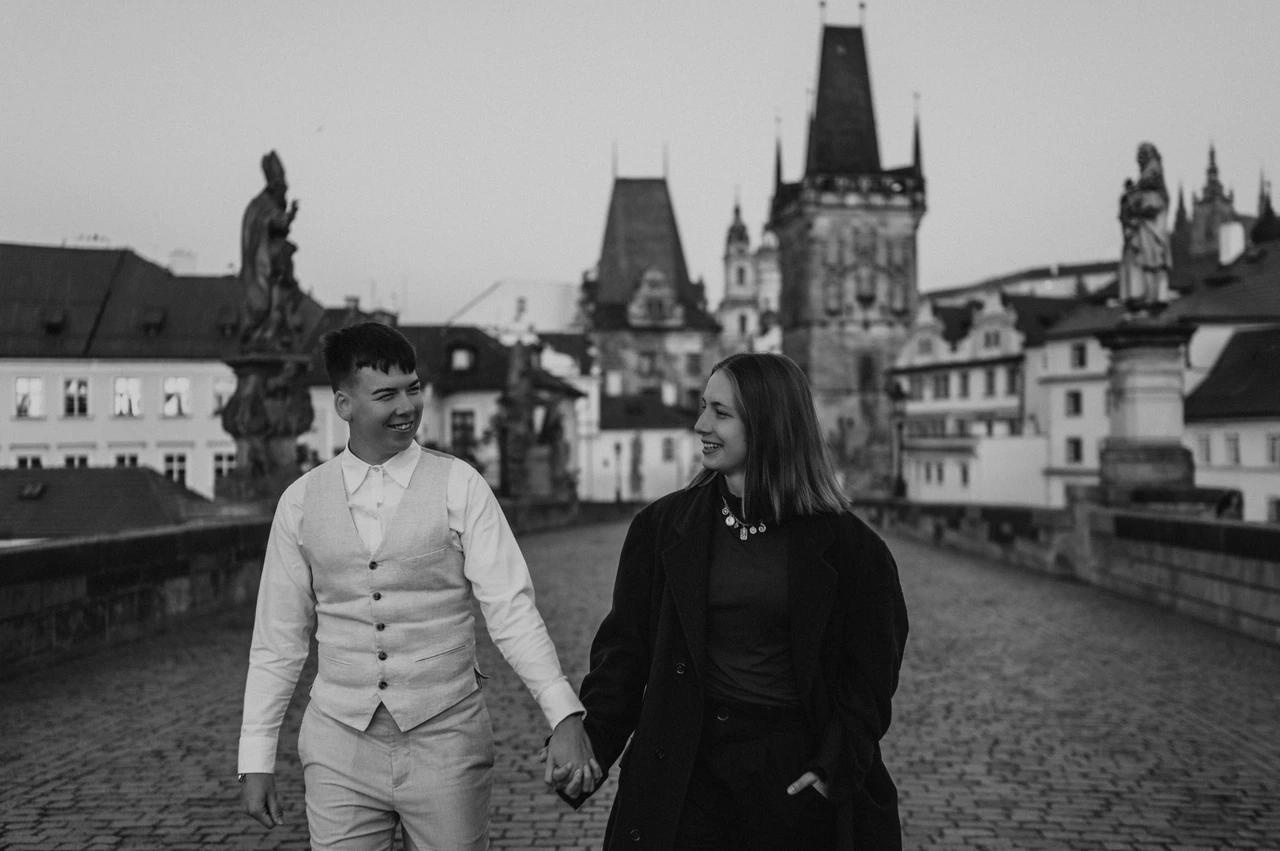 Prague couple photoshoot: black and white portrait of the couple walking on Charles Bridge. Black and white portrait of the couple walking on Charles Bridge during a couple photoshoot in Prague.