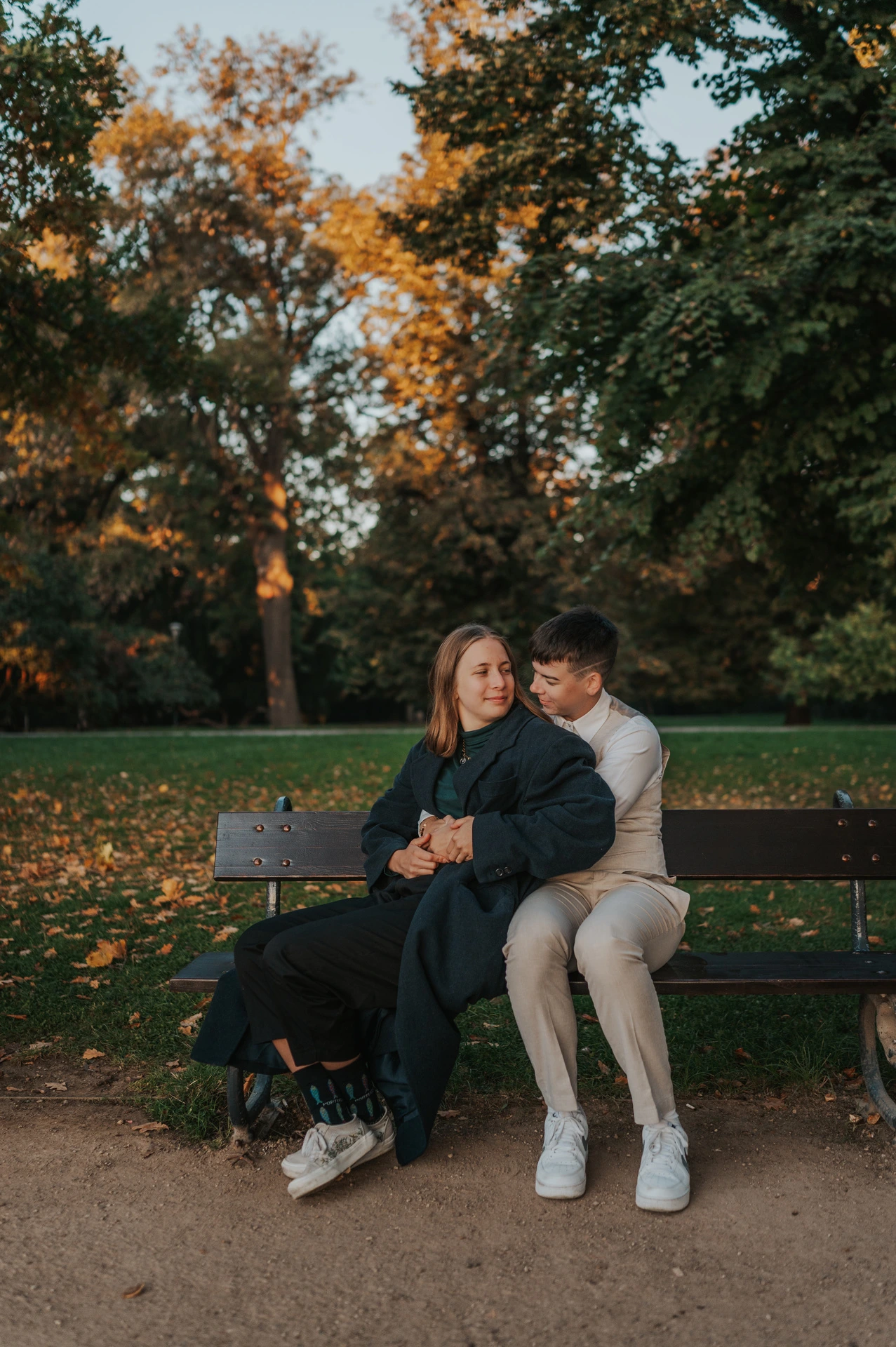 Couple cuddling on a park bench under autumn leaves during a couple photoshoot in Prague.