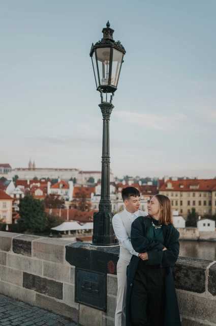 Prague couple photoshoot: couple embracing beneath a Charles Bridge street lamp. Couple embracing beneath a Charles Bridge street lamp during a couple photoshoot in Prague.