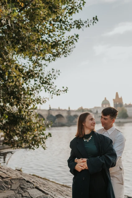 Prague couple photoshoot: couple embracing beneath the riverside trees. Couple embracing beneath the riverside trees during a couple photoshoot in Prague.