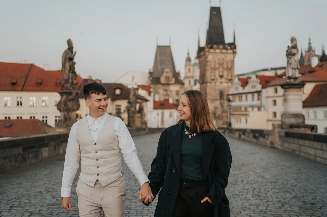 Prague couple photoshoot: couple exchanging smiles while walking on Charles Bridge. Couple exchanging smiles while walking on Charles Bridge during a couple photoshoot in Prague.