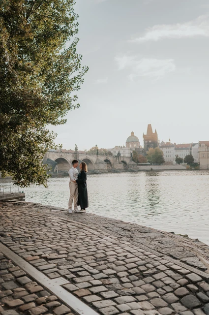 Prague couple photoshoot: couple holding each other on the tree-lined riverbank. Couple holding each other on the tree-lined riverbank during a couple photoshoot in Prague.