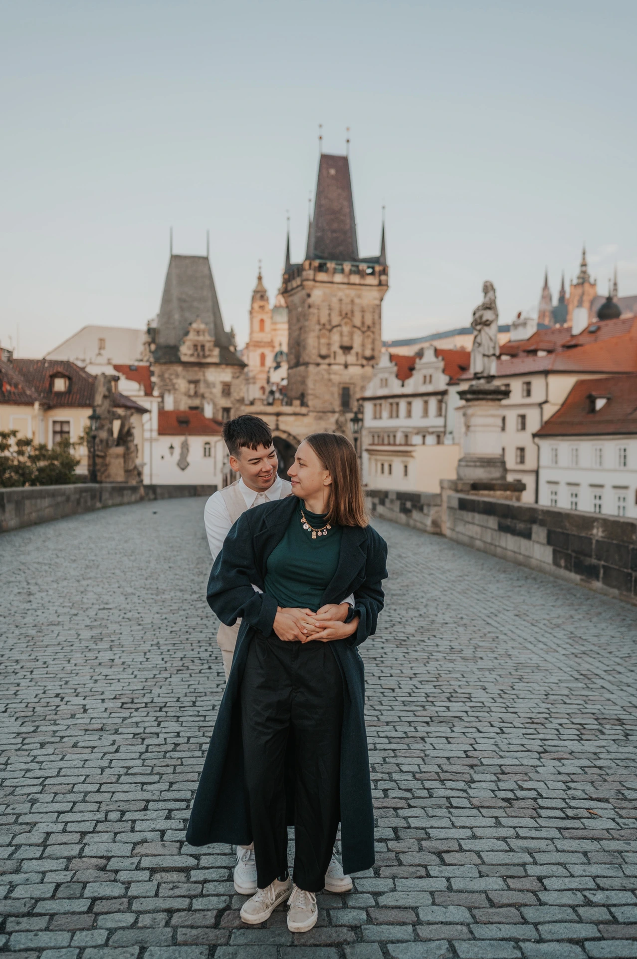 Couple holding each other with bridge towers behind them during a couple photoshoot in Prague.