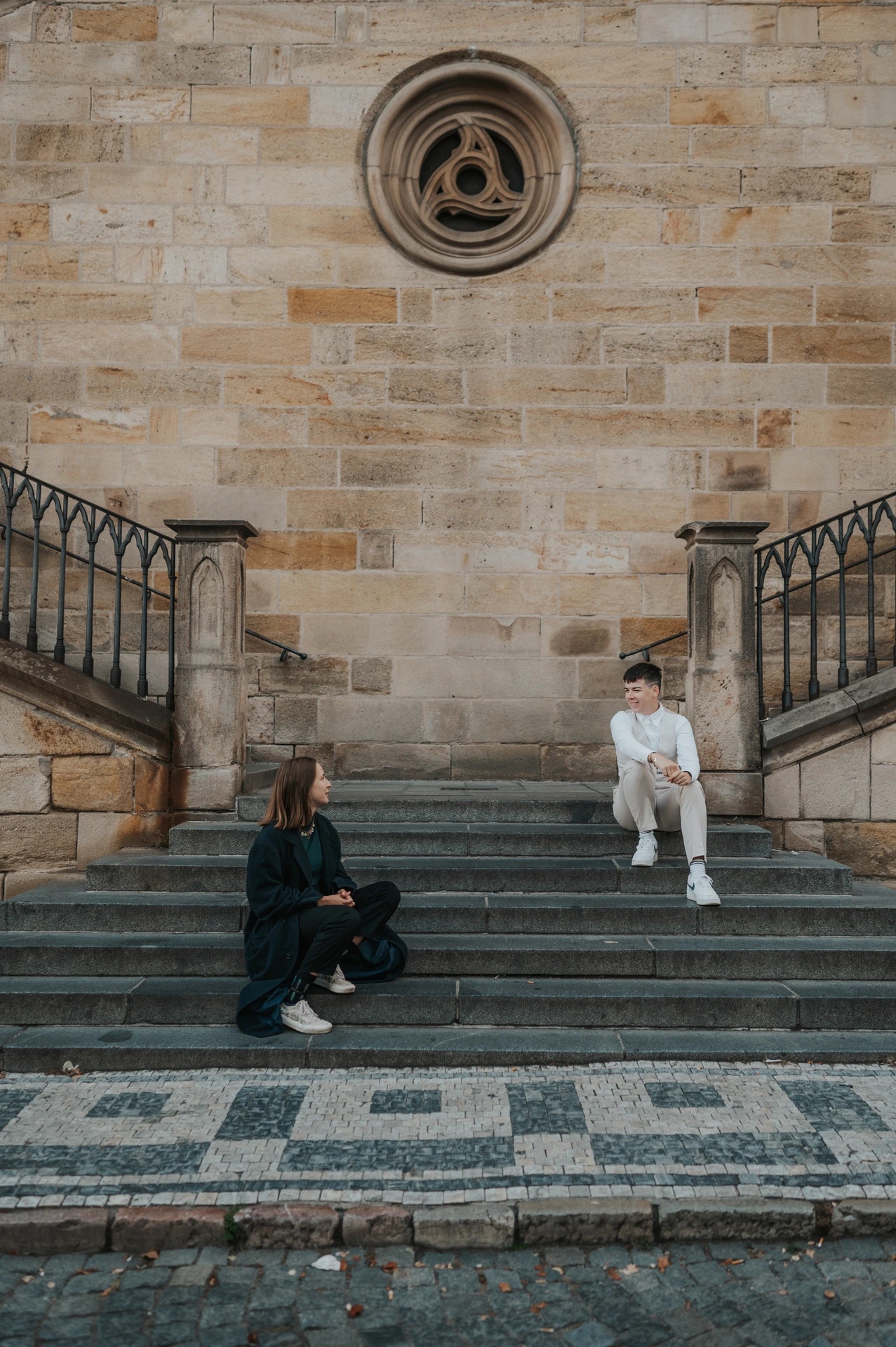 Couple sitting apart on the broad stone staircase during a couple photoshoot in Prague.