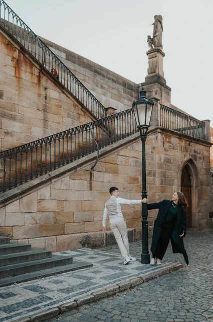 Prague couple photoshoot: couple smiling as they walk beside the bridge wall. Couple smiling as they walk beside the bridge wall during a couple photoshoot in Prague.