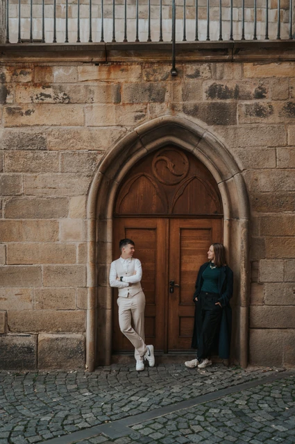 Prague couple photoshoot: couple standing either side of an arched wooden doorway. Couple standing either side of an arched wooden doorway during a couple photoshoot in Prague.