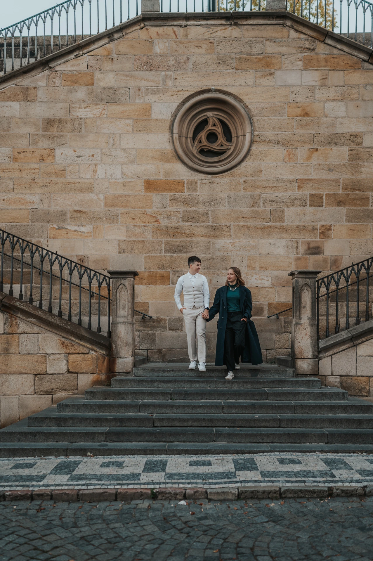 Couple standing together beneath a round stone window during a couple photoshoot in Prague.
