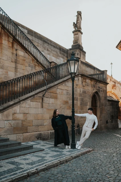Prague couple photoshoot: couple walking beside the Charles Bridge stairway. Couple walking beside the Charles Bridge stairway during a couple photoshoot in Prague.