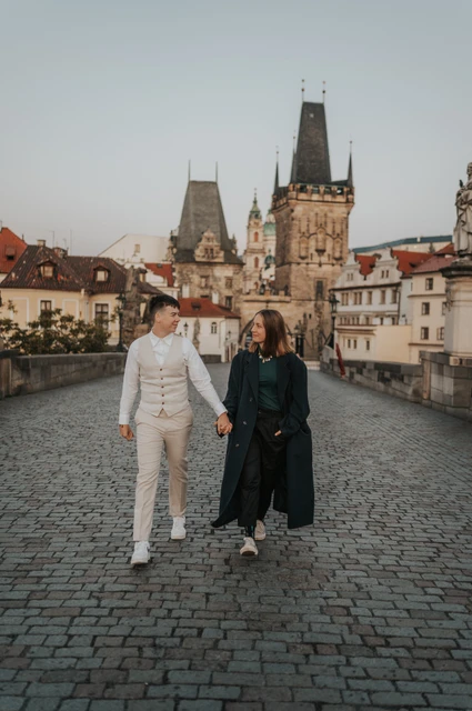 Prague couple photoshoot: couple walking hand in hand towards the Charles Bridge towers. Couple walking hand in hand towards the Charles Bridge towers during a couple photoshoot in Prague.