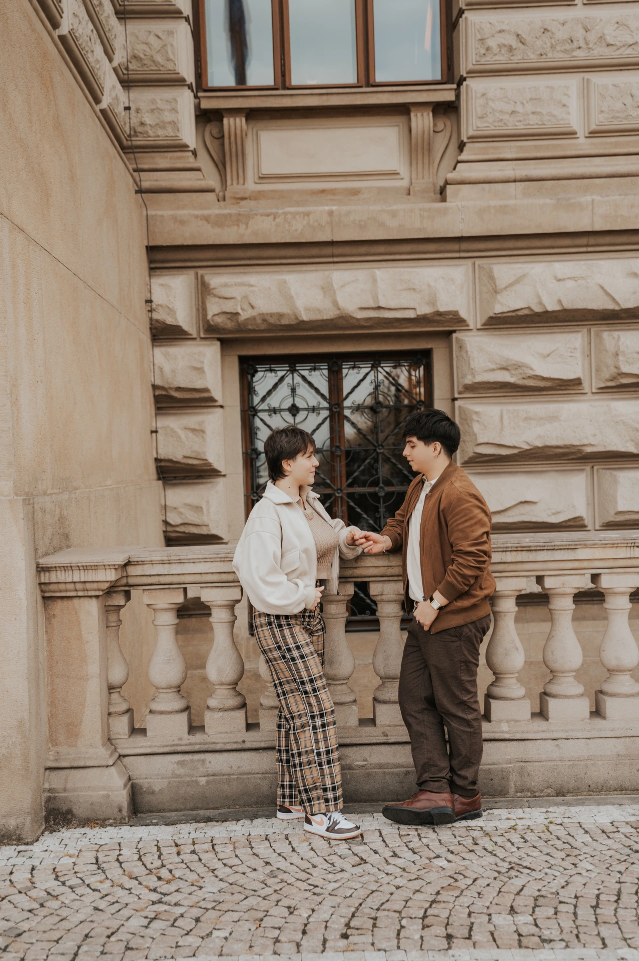 Couple facing each other beside a carved museum window during a couple photoshoot in Prague.