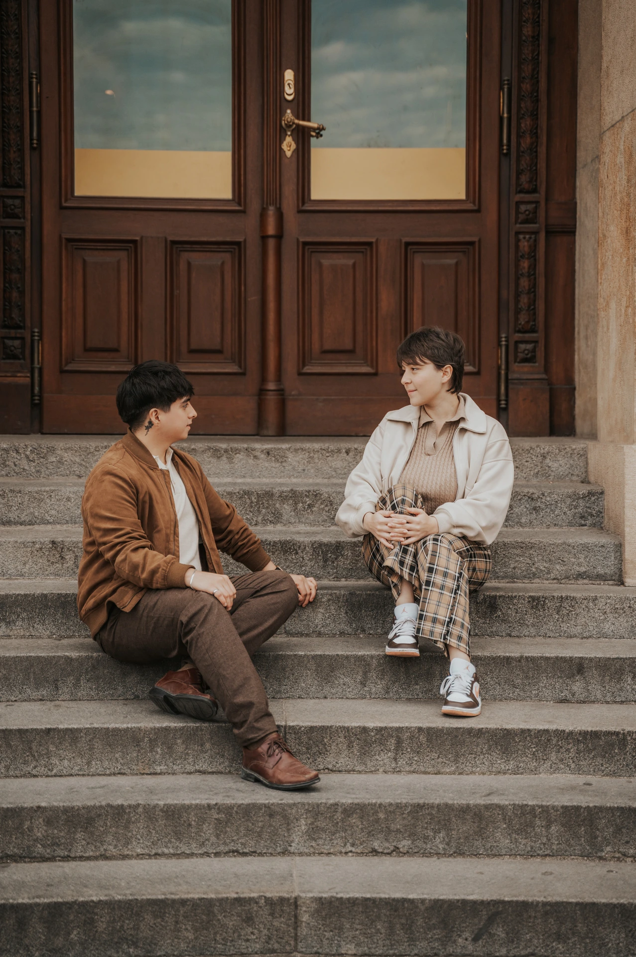 Couple sitting on the steps beneath wooden doors during a couple photoshoot in Prague.
