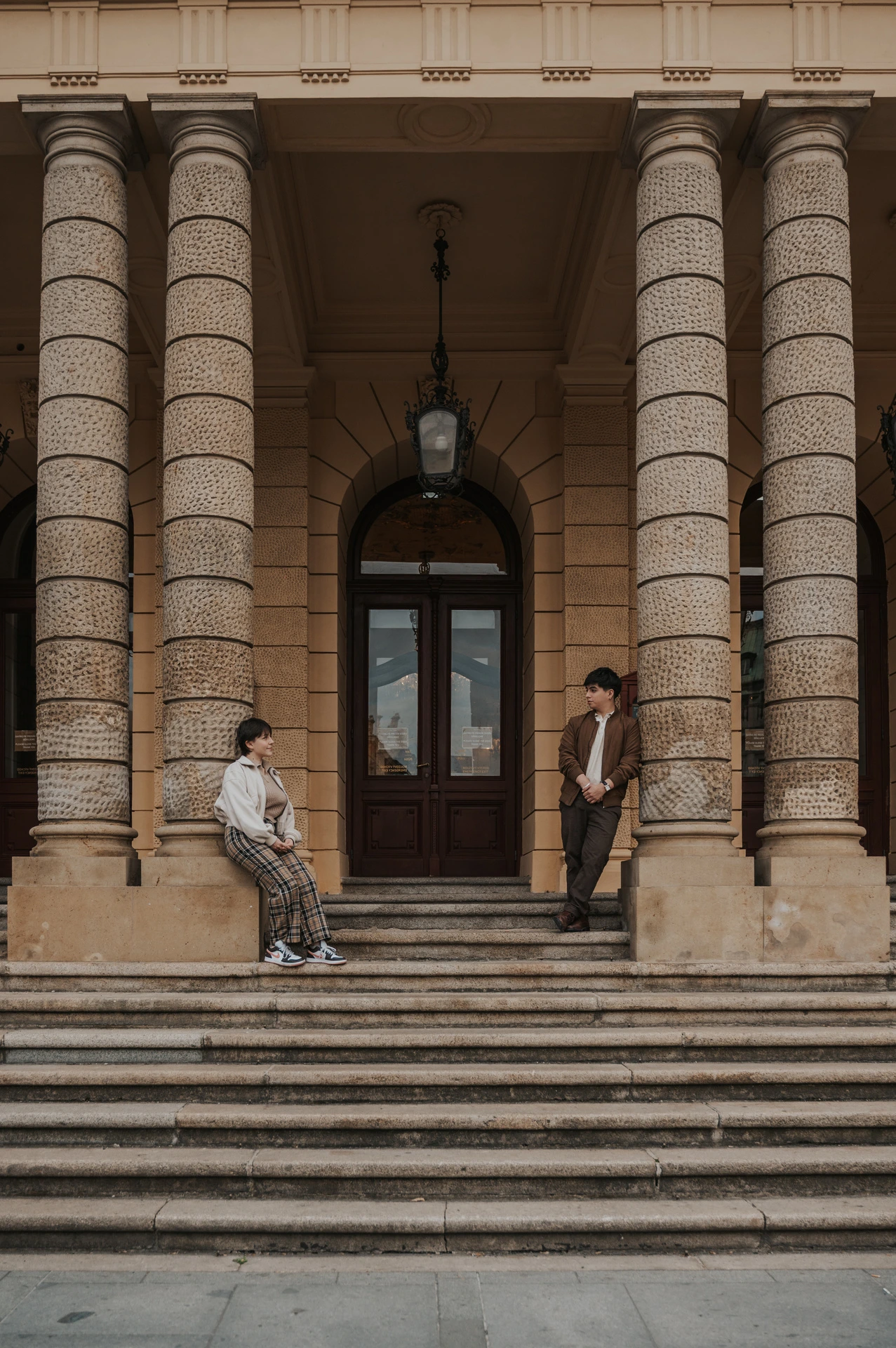 Couple standing apart on the steps between stone columns during a couple photoshoot in Prague.